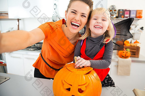 笑万圣节穿着女孩年轻的妈妈。使自拍大橙色南瓜南瓜灯装饰厨房传统的秋天假期