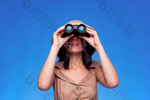 一个戴着木髓头盔的女人用一副双筒望远镜在蓝色背景下搜索，并留有空间