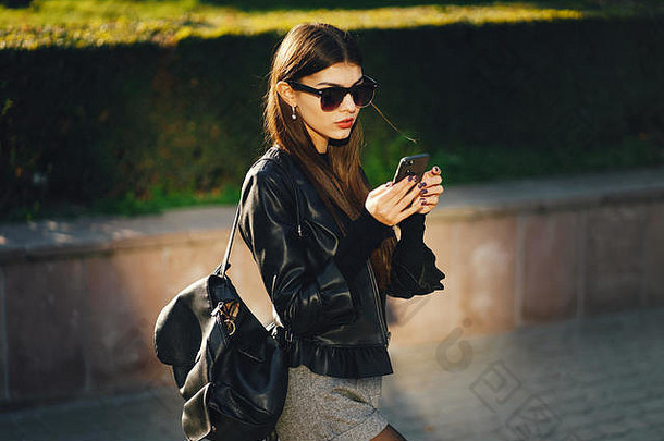 时尚女孩一边用手机一边在城市里走来走去