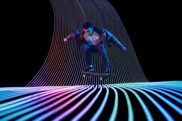 白种人年轻的滑板运动员，骑在黑暗的霓虹灯背景上。在彩色波浪上进行动作训练。爱好的概念，健康的生活方式，青春，行动，运动，现代风格。