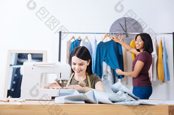 当她的同事站在她背后时，一位熟练的年轻女子正在缝纫