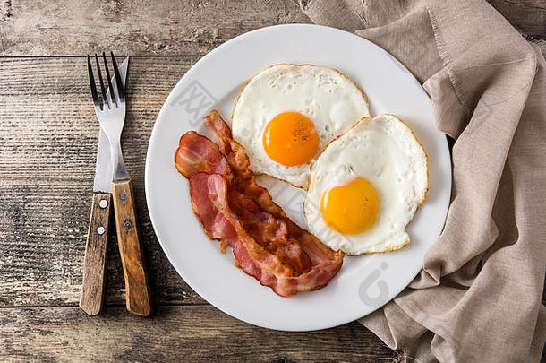 早餐在木桌上煎鸡蛋和熏肉。俯视图