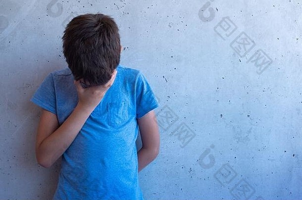 伤心的男孩独自站在灰色的墙上。学习困难、家庭问题、欺负、抑郁、压力或挫折概念