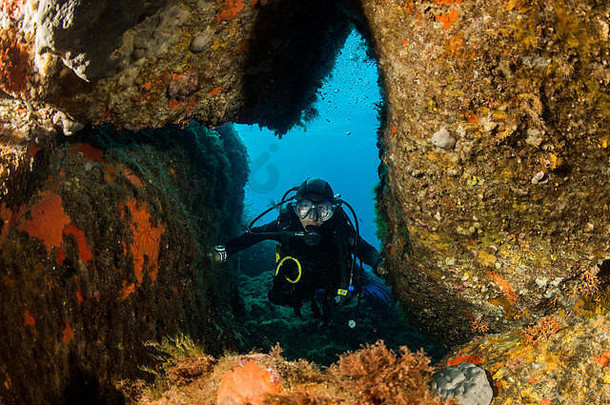 在地中海的一个洞穴里，一名女子戴着水肺在岩石上潜水
