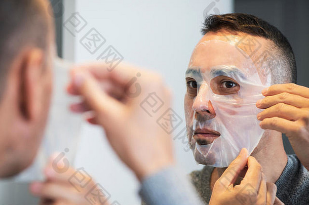 特写镜头：一位英俊的白人男子在自己脸上涂上生物纤维<strong>素面</strong>膜