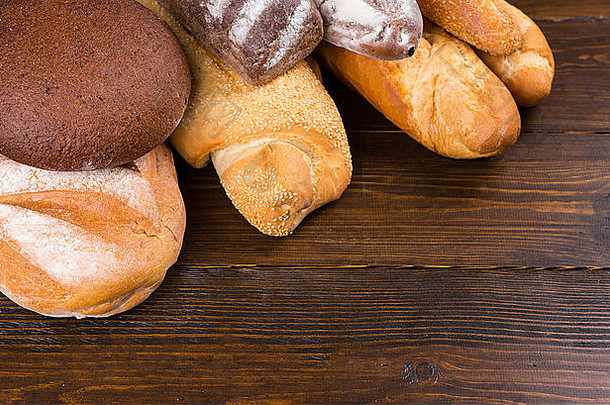 深色木桌上全法国面包和黑麦面包末端的特写镜头，上面覆盖着面粉