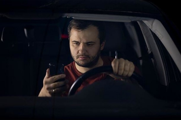 悲伤的司机晚上坐在车旁，疲惫地看着智能手机，担心出现问题
