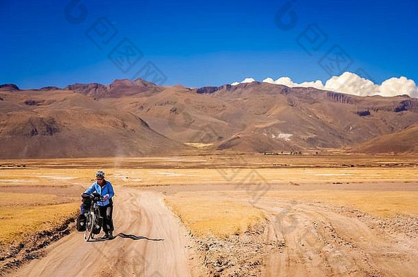 玻利维亚Altiplano，一名骑自行车的妇女在沙质瓦楞路上挣扎着推着自行车