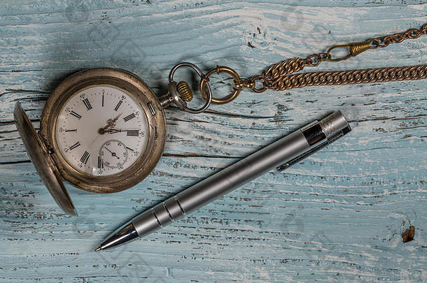 木制桌子上的旧银怀表和钢笔