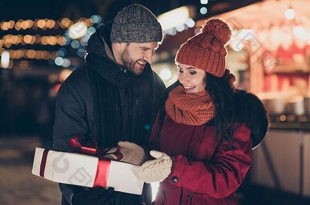这张照片是一个家伙在<strong>户外</strong>给<strong>美</strong>女送圣诞礼物盒，上面有红结的<strong>新年</strong>传统，穿着保暖外套、针织帽子和围巾