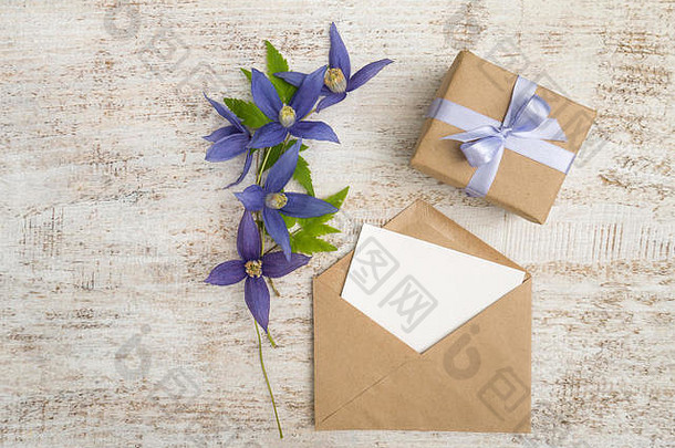 用棕色牛皮纸包裹的礼品盒，带有紫色缎面蝴蝶结、蓝色花朵和信封，信封上印有木制彩绘的贺卡