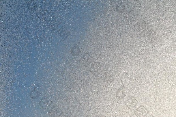 蓝色窗户玻璃覆盖着白霜冰纹纹理。寒冷的自然冬季背景。