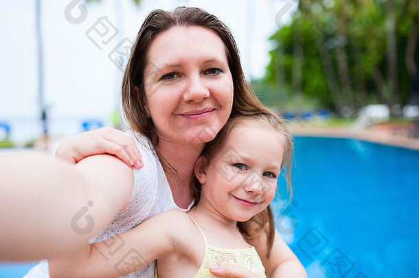 快乐的妈妈和她可爱的小女儿在游泳池附近的户外进行自拍
