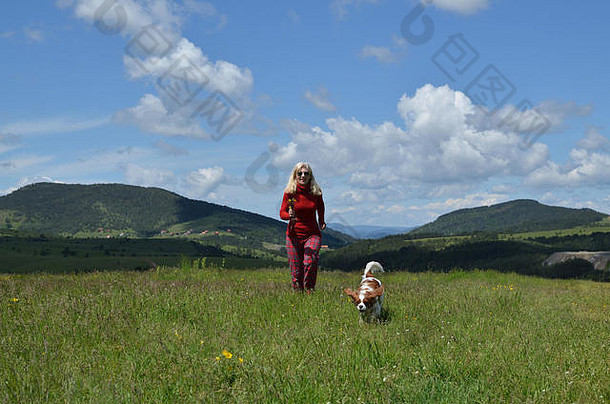 女人穿着<strong>红色</strong>的狗骑士王查尔斯猎犬运行山草地景观背景