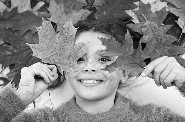 孩子们喜欢秋天。可爱的小女孩躺在橙色的落叶背景上。干枫叶在她的发型。秋季概念。秋季护发小贴士和想法。她心里想着秋天。