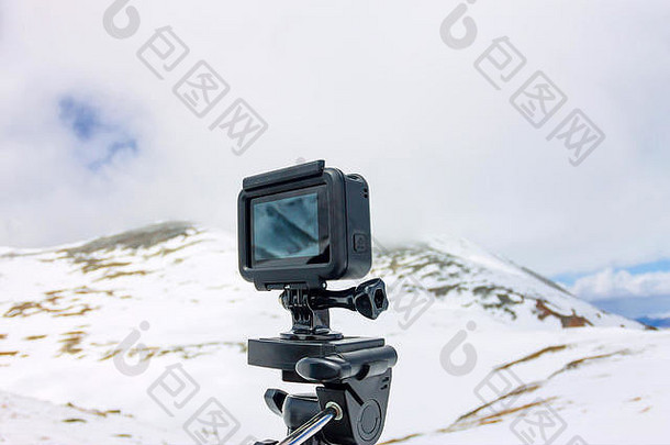 动作摄像机站在山的背景下的三脚架上。