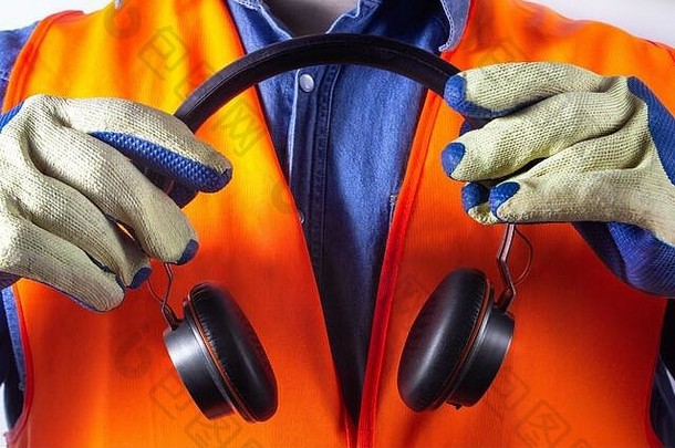 身穿橙色夹克的工人戴着防护手套，手持白色背景的音乐耳机。