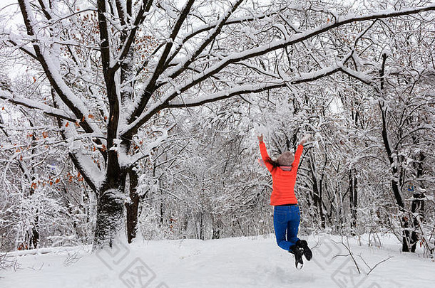 冬天，一个年轻漂亮的女孩穿着鲜艳的<strong>珊瑚色</strong>夹克和蓝<strong>色</strong>牛仔裤，在胸罩附近的白雪覆盖的童话森林里漫步