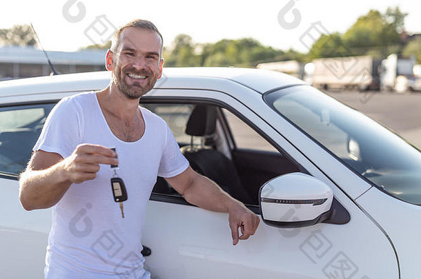 一名男司机站在一辆车旁边，手里拿着钥匙，微笑着。