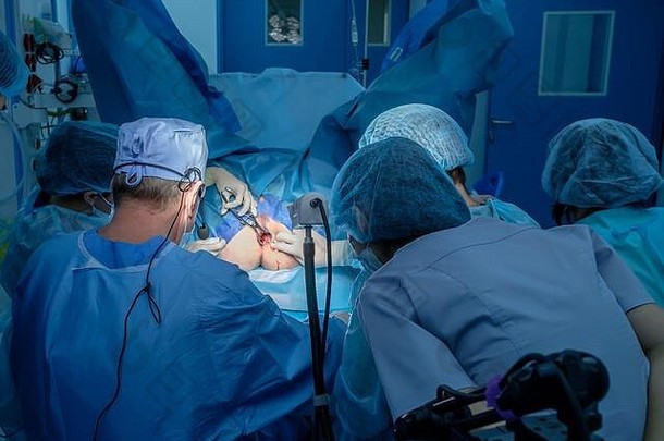 一组外科医生使用手术器械对病人的肛门进行<strong>微创</strong>手术。外科医生有无菌的蓝色手术服