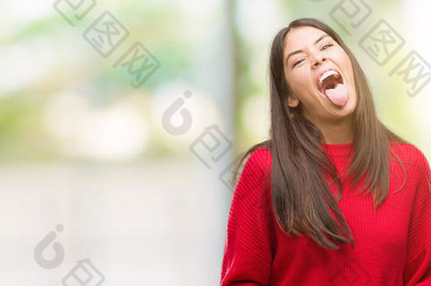 年轻漂亮的西班牙裔，穿着红色毛衣，露出快乐的舌头，表情滑稽。情感概念。