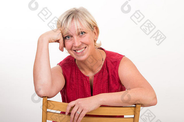 美丽的欧洲中年妇女穿着红色连衣裙，轻松地坐在木椅上——摄影棚在白色背景前拍摄