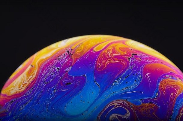 这张迷幻彩虹的特写镜头在肥皂泡中混合和旋转，看起来像一个被黑色背景隔离的幻想星系或行星