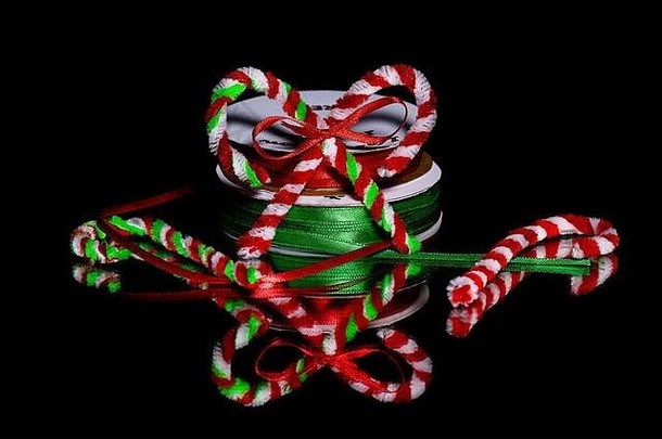 节日工艺品、管道清洁剂糖果手杖，在黑色反光表面上，黑色背景下有红色和绿色丝带缠绕。有c的空间