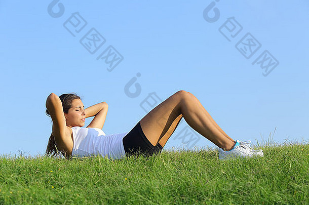漂亮的女人仰卧起坐绿色草天空背景