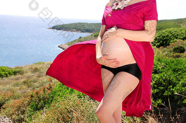 美丽的孕妇和女士站在自然环境中，抱着她怀孕的肚子。等待婴儿。妈妈牵着贝尔的手