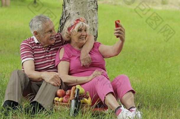 家庭周末野餐人高级高加索人夫妇智能手机视频调用会说话的网络摄像头聊天社会媒体网络电话上了年纪的男人。女人丈夫妻子公园