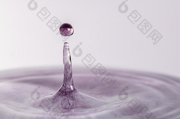 一个紫色水滴在浅色白灰色背景下溅入水中的特写微距摄影