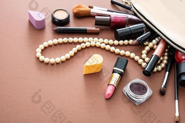 用专业配件制作化妆包。唇膏和刷子从棕色背景下的金色化妆包中取出，空间。