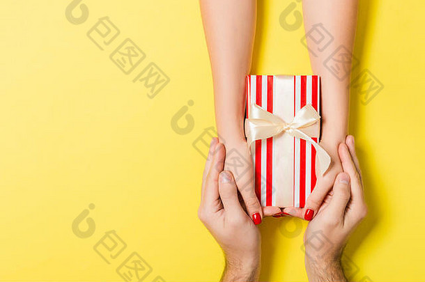 彩色背景下，男女手持礼品盒的俯视图。分享礼物的概念。闭合。