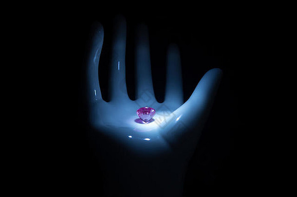 钻石宝石。美丽的粉红色明亮图像，在黑色背景上，手掌上有反射面。