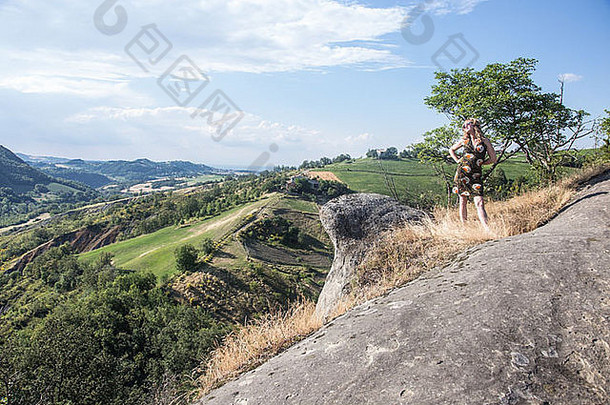 穿着裙子的金发女人站在岩石上，眺望着乡村山谷，眺望着远方