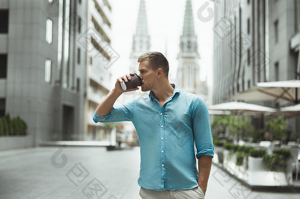年轻英俊的男子边走边喝咖啡，在市中心的街道上散步，感觉很快乐