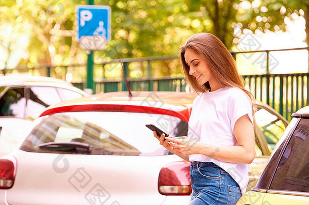 这张照片拍摄的是一名年轻女子站在汽车旁边的街道上，通过<strong>手机支付</strong>停车费。