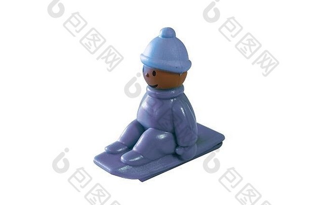 一个孩子坐在雪橇上下山，戴着帽子御寒，连指手套紧紧地抓着雪撬，这是一个给小孩子的彩色小玩具