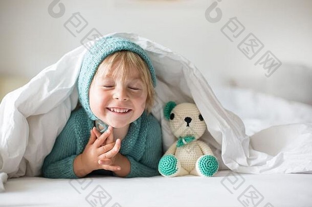 可爱的蹒跚学步的小男孩，带着手工编织的玩具，躺在床上，开心地微笑着