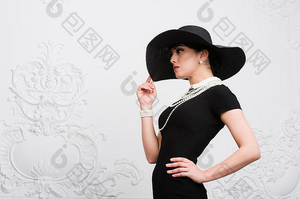 复古风格的美丽年轻女子肖像，戴着优雅的黑色帽子，穿着奢华的罗科科科墙饰