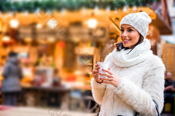 一位美丽的年轻女子正在<strong>圣诞</strong>集市上享用一杯热葡萄酒。