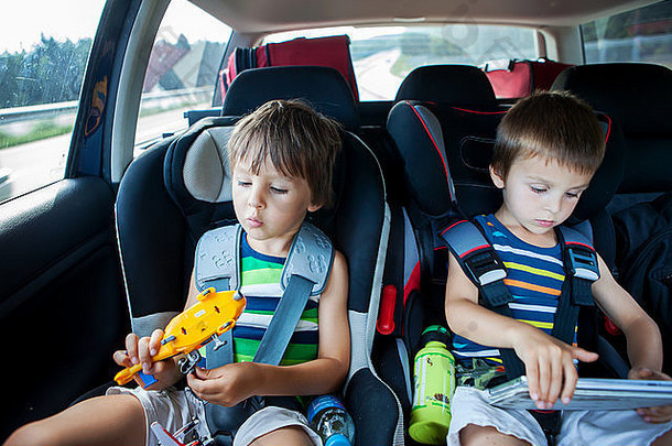两个男孩坐在<strong>儿童汽车</strong>座椅上，开车旅行，玩玩具和平板电脑，夏天