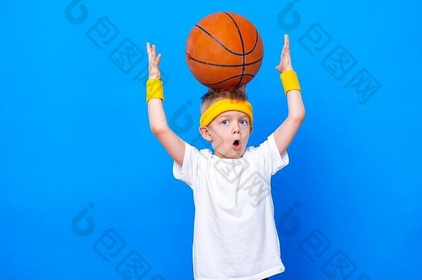 蓝色演播室背景上有篮球的运动型小男孩。体育锻炼。儿童运动员。活动运动健身、健康和活力。成功