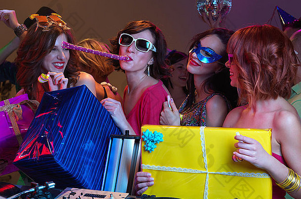 一群美丽的女孩玩着派对号角笑着的特写镜头。人们在背景下跳舞