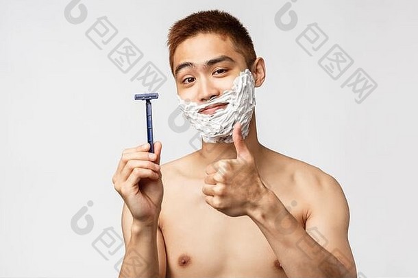 美、人、卫生理念。喜气洋洋的亚洲帅哥推荐剃须刀或剃须膏，脸朝里的时候高兴地竖起大拇指微笑