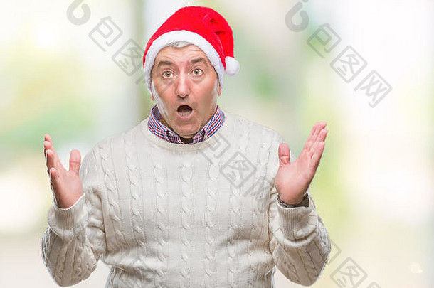 英俊的老人戴着圣诞帽，在孤立的背景下疯狂地<strong>大</strong>喊<strong>大</strong>叫，表情咄咄人，双臂高举。Frus