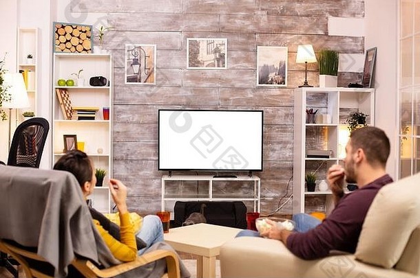在舒适的客厅里，一对夫妇一边吃外卖，一边看着隔离的电视屏幕