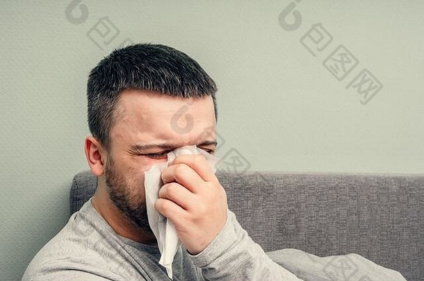 病在家里欢呼。一个年轻人生病了，在家里接受治疗。用餐巾纸擤鼻子，流鼻涕。传染病，流行病，芽孢杆菌携带者。