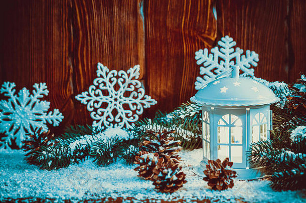 用蜡烛、圣诞树枝、圆锥体、雪花和雪在复古木背景上点亮的圣诞灯笼。自由空间